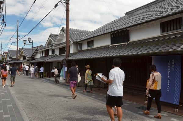 右側に5軒ほどの日本家屋が並んでいて、その手前にある道路を10名以上の人達が歩いている写真